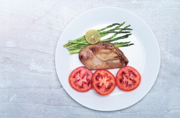 Healthy food chicken grill with lemon and asparagus tomato in plate on white wood background top view.