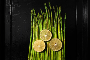 Healthy food asparagus grill with lemon in black tray top view.