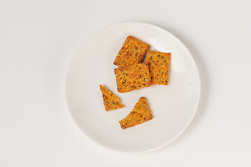 Eaten square vegetable crackers with spices in white plate isolated on white, top view
