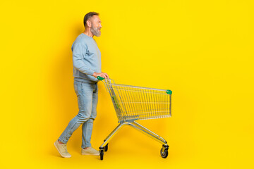 Full length profile portrait of aged person push shopping car look empty space isolated on yellow...