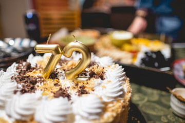 Moka cream birthday cake with '72' number golden candles in a party