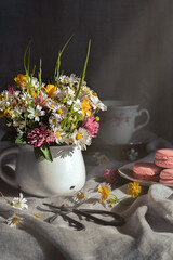 Wild flowers in white mug, sweets und cup of tea on grey background.Rustic template for postcard.Women's day, Mothers Day  concept.Imitation of  an old photo.