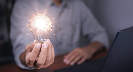 The hand of a man with a light bulb and there is a brain icon in it and he is using a notebook computer. the idea of ​​inspiration from online technology. different ideas and innovation idea concept.