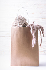 Craft unbranded paper bag with goods such as woolen scarf and hat on rustic wooden background close up. Black Friday sale banner, copy space for your design.