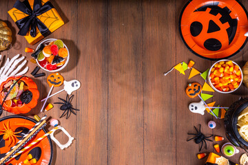 Halloween sweets and snacks table. Set of Halloween dinner party foods, candy, snacks, with holiday costume decorations, pumpkin buckets, wooden background top view copy space