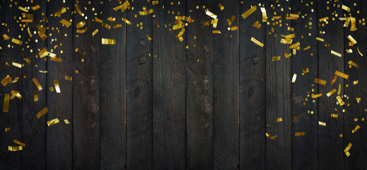 Golden glittering confetti on dark wooden planks.Top view on rustic wood surface with confetti...