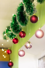 Fototapeta na wymiar Christmas decor above the window. Green garland and balls of red and pink color