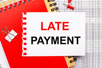 Against the background of the reports, there are red and brown notepads, a white paper clip, red buttons and a white sheet of paper with the text LATE PAYMENT. Business concept