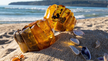 Two shiny orange Baltic amber bracelets  close up on the sand. Amber jewelry is near the sea. 