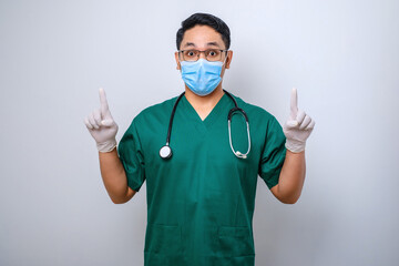 Surprised or curious male nurse in green scrubs, medical mask, pointing fingers up, inform patients how prevent corona infection