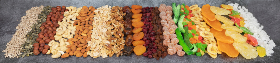 Food horizontal banner with a healthy snack. Candied fruits, dried berries, nuts, seeds on a dark background top view. Vegetarian mix of vitamin food