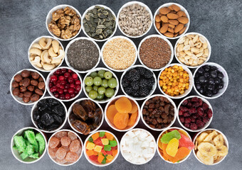 Berries, nuts, seeds, dried fruits in round containers. Background with a mix of healthy snacks. Assorted vitamin food on a grey background.