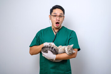Shocked doctor in vet clinic examining cat with stethoscope, gasping amazed while holding cat in his arm