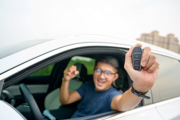 A handsome young man in a good mood holding the keys to his new car with a smile. Asian man with car keys in hand. concept of having a new car
