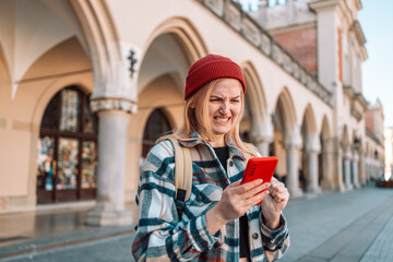 sad angry woman with blonde hair annoyed by something while using phone, girl has received bad sms, text message in old city street. Emotion, reaction, feeling. High quality photo