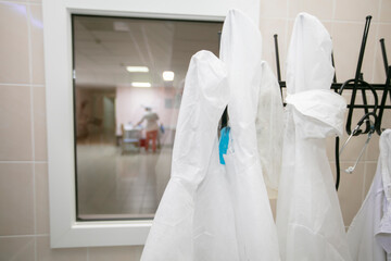 White medical gowns hang on hangers in the hospital.