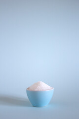 white sugar in a blue bowl on a light blue background