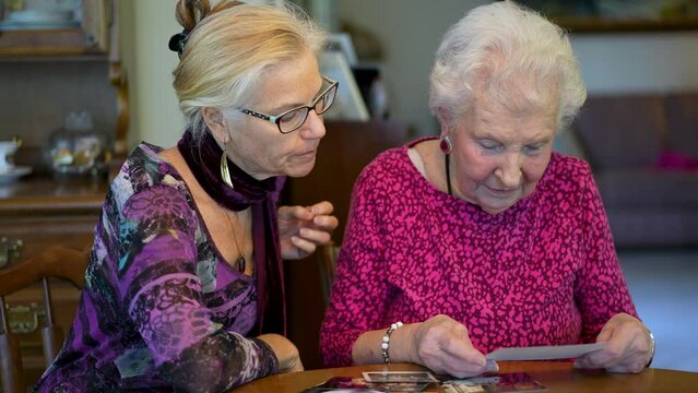 Elderly woman looks at photos with daughter. Senior woman sitting in the dining room looking at photographs with daughter. Brain training. Memory activity.