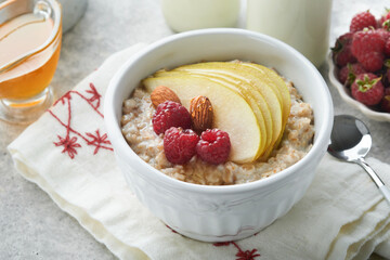 Oatmeal. Bowl of oatmeal porridge with raspberry, pear and honey on gray concrete old table background. Hot and healthy food for Breakfast, top view, flat lay