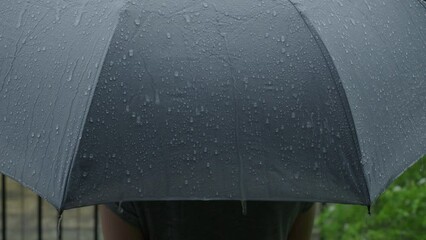 Rain on grey umbrella. Silver umbrella in the rain on evening Bangkok. Footage rain drops falling on umbrella. Represent bad weather winter rainy season or protection. Person and umbrella in the rain.