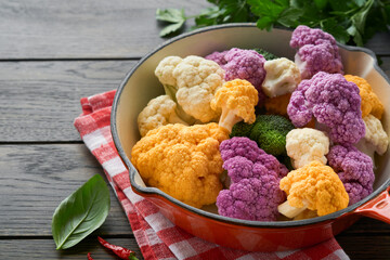 Colorfu cauliflower. Cauliflower cut into small pieces in red iron panon old wooden rustic background. Food cooking and agricultural harvest concept or background.