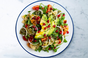 Argula salad with pasta bows, avocado, cherry tomatoes, pomegranate and sesame.