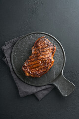 Steaks. Grilled New York Steak with spices rosemary and pepper on black marble board on gray background. Top view. Mock up.