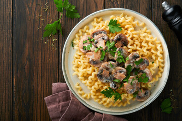 Fusilli pasta with mushrooms, cheese and garlic creamy sauce on plate on old wooden dark table background. Top view. Traditional Italian cuisine.