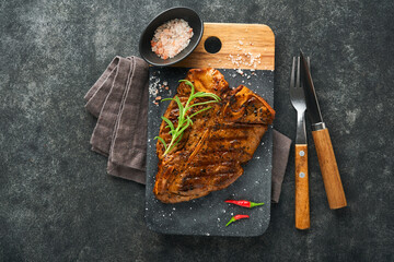 Raw steak t-bone or porterhouse. Steak t-bone or porterhouse in sauce with spices, salt and rosemary on a black ceramic plate on concrete background. Top view. Place for text.