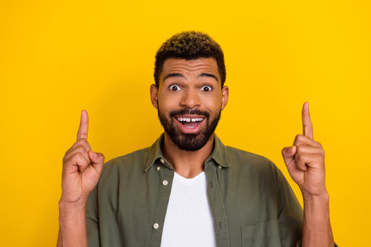 Photo of funny impressed man wear khaki shirt pointing up empty space isolated yellow color background