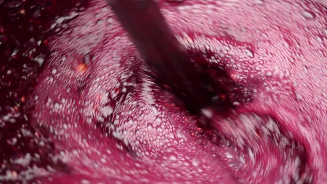 Stirring red grape must in a barrel, showcasing the vibrant color and texture during winemaking