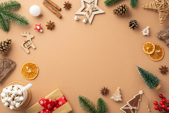 Top view photo of christmas decorations wood ornaments giftbox cup of cocoa mistletoe pine cones branches bark cinnamon dried orange slices on isolated beige background with copyspace in the middle