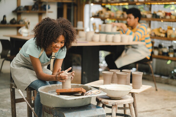 Fototapeta premium Creative afro American young woman artist molding clay on pottery wheel, Workshop in ceramic studio, clay making of a ceramic pot on the pottery wheel, hobby and leisure with pleasure concept