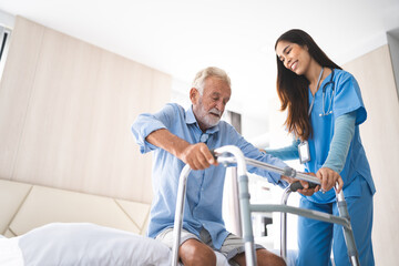 Portrait of Asian young nurse helping old elderly disable man grandfather to walk by using walker equipment in the bedroom. Senior patient of nursing home moving with walking frame and nurse support