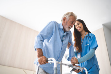 Fototapeta premium Portrait of Asian young nurse helping old elderly disable man grandfather to walk by using walker equipment in the bedroom. Senior patient of nursing home moving with walking frame and nurse support
