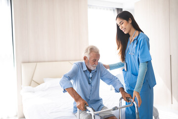 Fototapeta premium Portrait of Asian young nurse helping old elderly disable man grandfather to walk by using walker equipment in the bedroom. Senior patient of nursing home moving with walking frame and nurse support