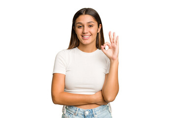 Young Indian woman isolated cutout removal background winks an eye and holds an okay gesture with hand.