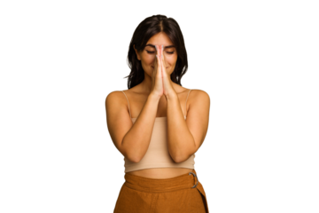 Young Indian woman isolated on green chroma background holding hands in pray near mouth, feels confident.
