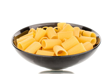 Several raw yellow cannelloni in a black ceramic plate, macro, isolated on white background.