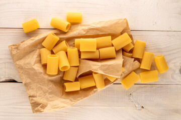 Several raw yellow cannelloni on a paper bag on a wooden table, macro, top view.