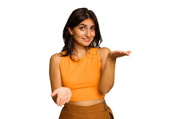 Young Indian woman isolated on green chroma background makes scale with arms, feels happy and...