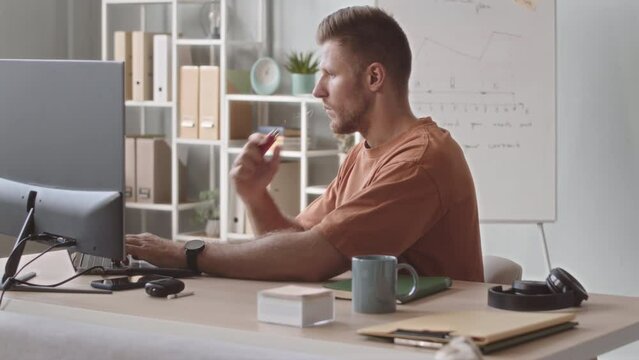 Waist up slowmo of Caucasian man smoking electronic cigarette while working on computer in office