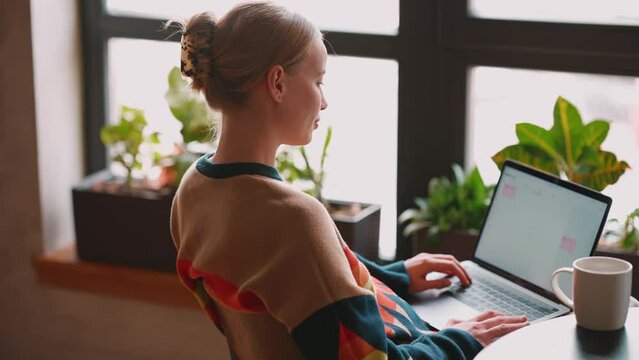Positive blonde woman working on laptop and drinking coffee in cafe