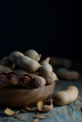 Tamarind fruit is placed in a wooden bowl and put on a rustic wooden floor.