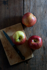Red apples with a kitchen knife and wooden cutting board on a rustic wooden floor, top view.