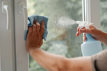 Man in casual clothes washing window glass at home. man's hand wipes the window with a blue...