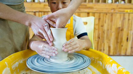 Potter teaching child to make ceramic pot on the pottery wheel
