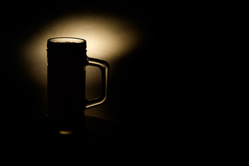 A glass of beer in the backlight , isolated on black smoke background . With space for text  - obrazy, fototapety, plakaty