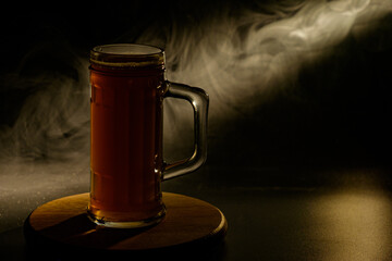 A glass of beer in the backlight , isolated on black smoke background . With space for text 