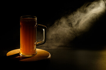 A glass of beer in the backlight , isolated on black smoke background . With space for text 